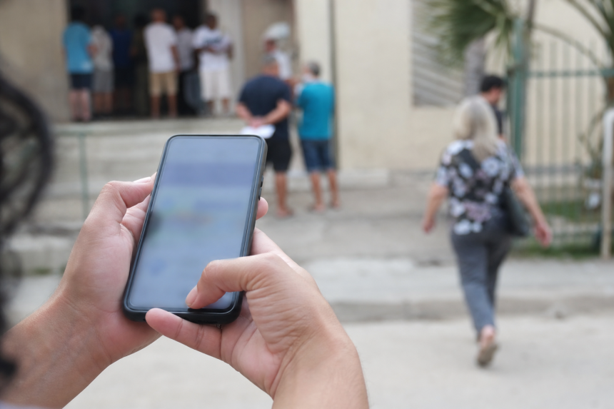 Pessoa usando celular para consultar informações oficiais sobre as eleições diante de uma seção eleitoral