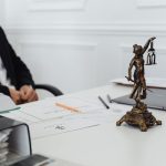 Mesa de trabalho jurídico com uma estátua da Justiça, documentos e um laptop.