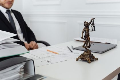 Mesa de trabalho jurídico com uma estátua da Justiça, documentos e um laptop.