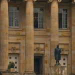 Fachada clássica de um edifício institucional com colunas e uma estátua na entrada.