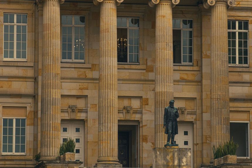 Fachada clássica de um edifício institucional com colunas e uma estátua na entrada.