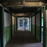 Corredor vazio de uma prisão, com portas de celas abertas e iluminação institucional.