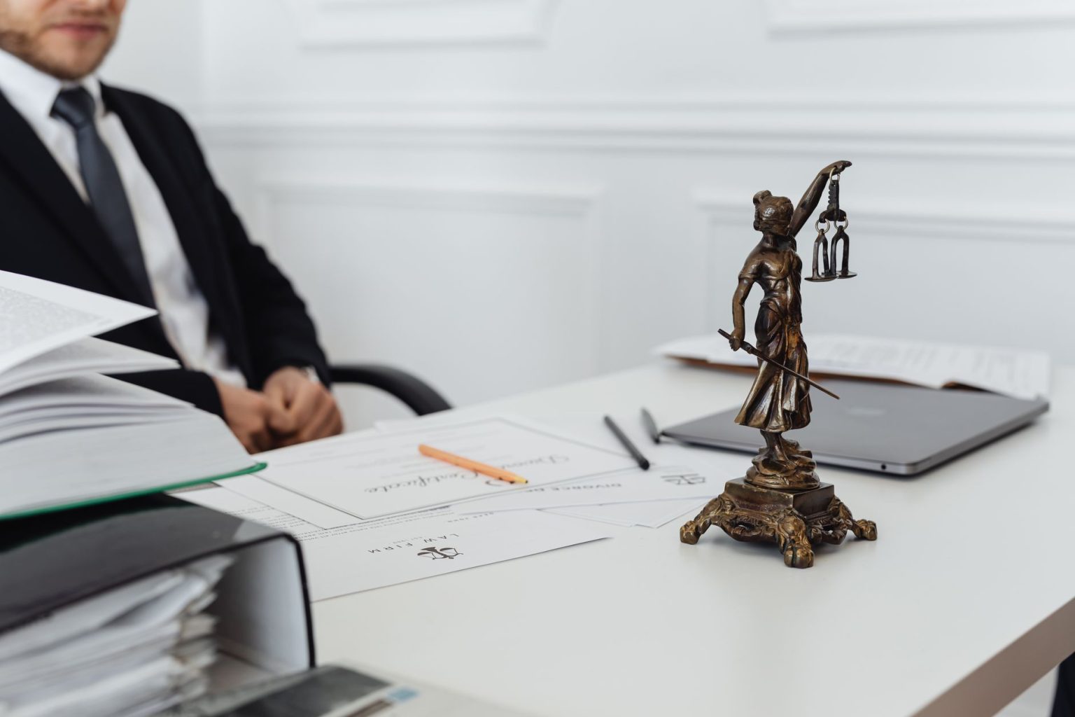 Mesa de trabalho jurídico com estátua da Justiça, documentos e um laptop.