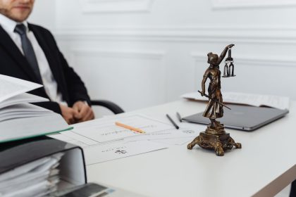 Mesa de trabalho jurídico com estátua da Justiça, documentos e um laptop.
