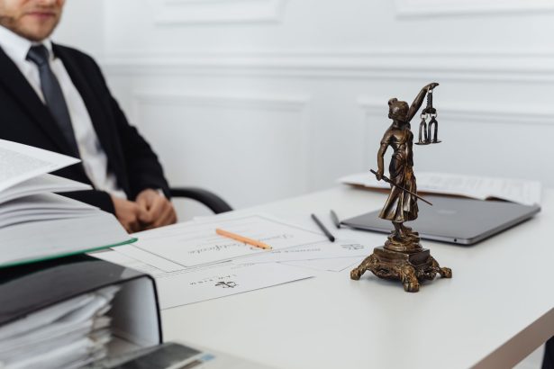 Mesa de trabalho jurídico com estátua da Justiça, documentos e um laptop.