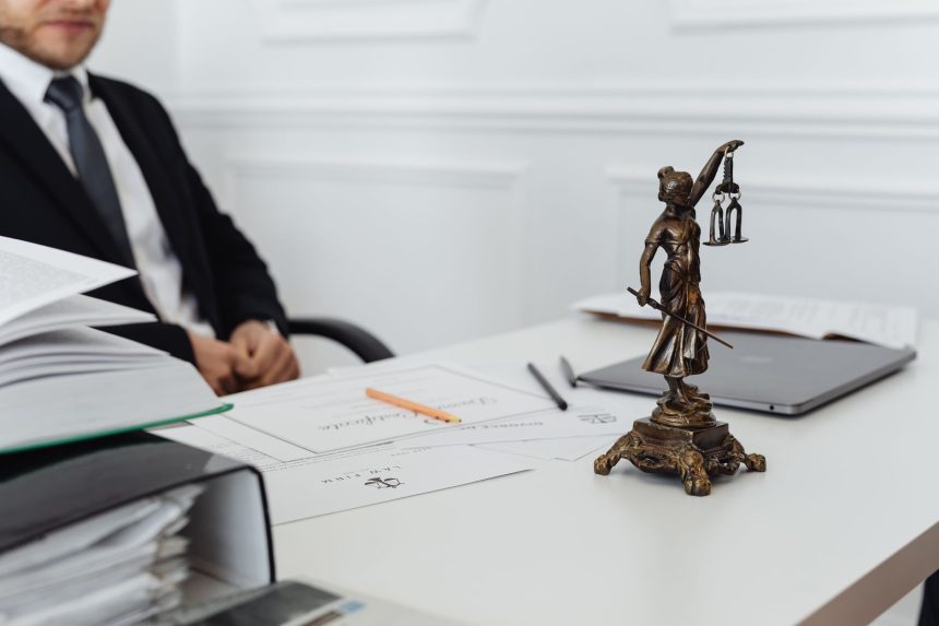 Mesa de trabalho jurídico com estátua da Justiça, documentos e um laptop.